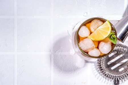 Rum, Lime and Cola Cuba Libre Cocktail. Summer cold  drink with citrus juice, ice cubes and mint leaves, white tiled sun lighted background copy spaceの写真素材