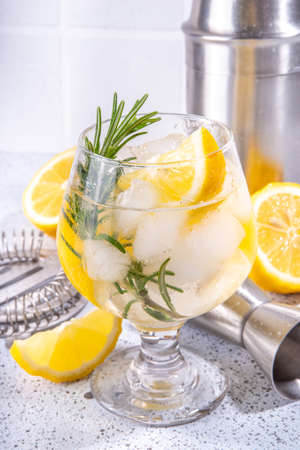 Infused rosemary lemon drink. Cold detox citrus lemonade with carbonated fizz water, lemon slices and rosemary sprig, white tiled background copy spaceの写真素材