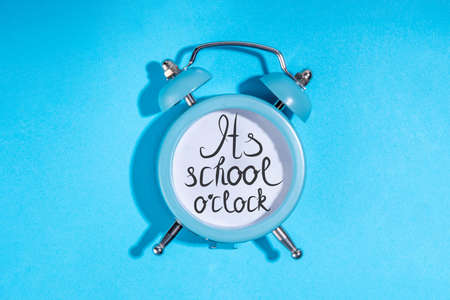 Back to school concept, simple minimal back to education background with small alarm clock with text Its school o'clock, on light blue background top view copy spaceの写真素材