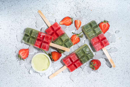 Dairy free green matcha and strawberry popsicles. Vegan ice cream popsicles with green matcha tea powder and dresh strawberry juice, Summer healthy organic dessert on white concrete backgroundの写真素材