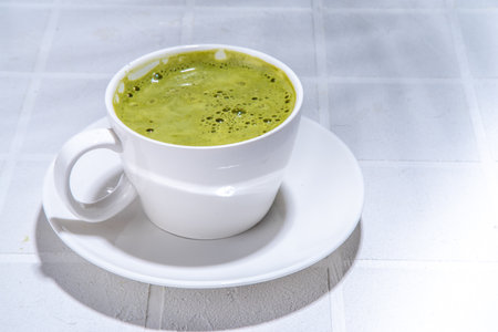 Matcha green tea latte on white concrete background with hard light, one cup of matcha drink in woman hands, top view copy spaceの写真素材