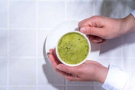 Matcha green tea latte on white concrete background with hard light, one cup of matcha drink in...