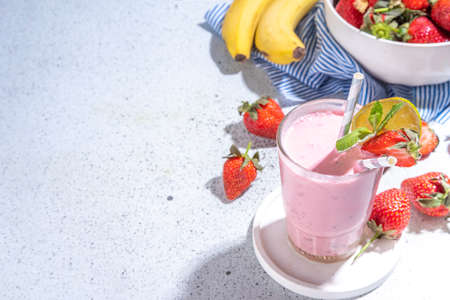 On glass with Strawberry banana milkshake, with fresh fruits on white concrete table, copy spaceの写真素材