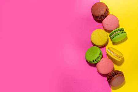 Bright colorful (yellow, pink, green, brown) various flavor macarons sweet cookies on high-colored pink yellow background. Stack of small french macaron cakes, copy space flatlayの写真素材