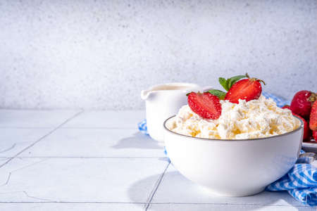 Bowl of homemade natural farm cottage cheese with fresh raw strawberry. Summer healthy diet balanced breakfast, morning snack, on white tiled background copy spaceの写真素材