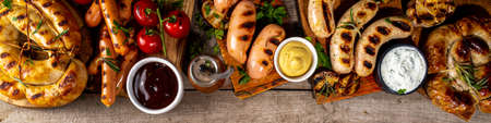 Mix bar-bq sausages - bavarian, round, gumberland, bratwurst with ketchup, mustard barbeque sauce. Various bbq grilled sausages flat lay on wood background. Street festival grill food menu.の写真素材