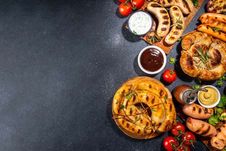 Mix bar-bq sausages - bavarian, round, gumberland, bratwurst with ketchup, mustard barbeque sauce. Various bbq grilled sausages flat lay on black background. Street festival grill food menuの写真素材