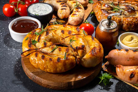 Mix bar-bq sausages - bavarian, round, gumberland, bratwurst with ketchup, mustard barbeque sauce. Various bbq grilled sausages flat lay on black background. Street festival grill food menuの写真素材