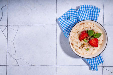 Rice porridge or pudding with fresh strawberry and nuts for breakfast, with plate of strawberries, white tiled background copy spaceの写真素材