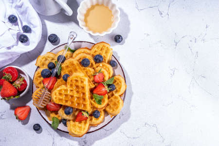 Breakfast belgian waffles with strawberries, blueberries and honey, homemade healthy heart shaped waffles on white kitchen tables copy spaceの写真素材