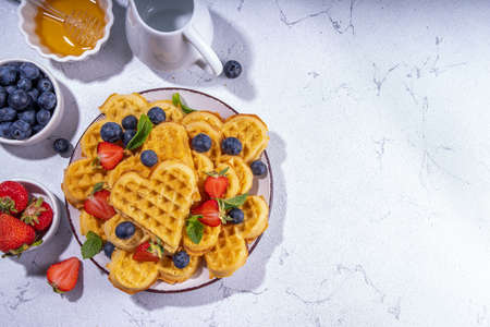 Breakfast belgian waffles with strawberries, blueberries and honey, homemade healthy heart shaped...