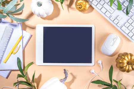 Simple pastel autumn office work, education flatlay top view copy space. Tablet with empty screen with fall holiday white and golden pumpkins, autumn decor leaves on beige high-colored backgroundの写真素材