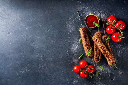 Shish kebab on skewers, from minced beef meat. Lula kebab, traditional Caucasian recipe. On black concrete background, with sauces, tomatoes and veggie salad top view copy spaceの写真素材