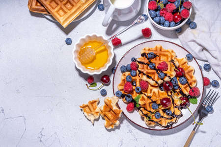 Sweet waffles with berries. Homemade summer breakfast belgian waffles with raspberries, blueberries, strawberry honey and chocolate dip sauce, copy spaceの写真素材