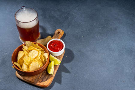 Beer with various salted snacks set. Black table background with traditional party snacks, beer bottles and glasses, with chips, onion rings, salted nuts, crisps and sauces top view copy spaceの写真素材