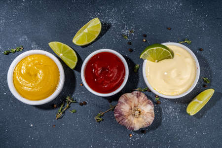 Classic set of sauces in white saucers: American yellow mustard, ketchup, mayonnaiseの写真素材
