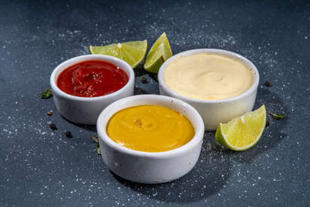 Classic set of sauces in white saucers: American yellow mustard, ketchup, mayonnaise