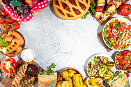 Various picnic barbeque food and drink flatlay. Summer bbq picnic food, assorted grilled meats, kebabs, vegetable, fruit salad, traditional picnic summer pie cake, sandwiches, top view copy spaceの写真素材
