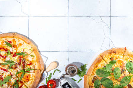 Three various pizzas, served at home or in restaurant on tiled table with cooking ingredients, tomato, basil, spinach, arugula Classic pepperoni pizza, vegetarian vegetable and seafood shrimp pizza,の写真素材