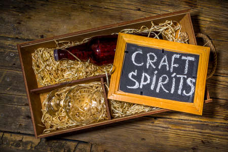 Craft spirit alcohol. Various bottles and glass with hand crafted hard strong alcohol drinks. Old wooden rustic background copy spaceの写真素材
