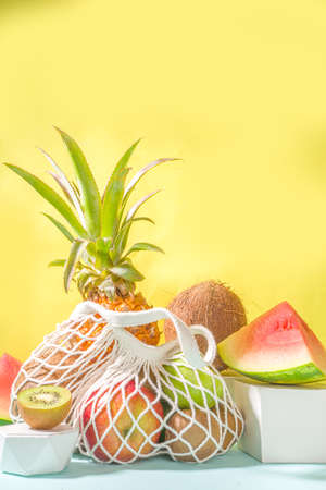 Summer fruit shopping background. Eco-friendly shopping bag full of fresh tropical fruits, on modern bright background with hard light copy space. Vitamin, healthy diet food conceptの写真素材