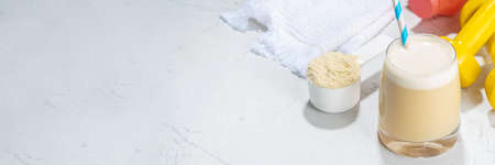 Vanilla white protein shake glass, with straw, with protein powder, dumbbell, towel and fitness accessories, on white sport bar table background copy spaceの写真素材