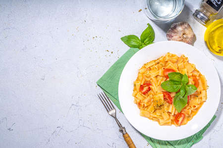Italian pasta lunch. Ready to eat cooked mini tortiglioni pasta with tomato cheese sauce, basil leaves and cherry tomato pieces. On white table with olive oil and spices,copy spaceの写真素材