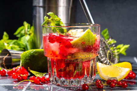 Red currant lemonade or mojito cocktail. Iced fresh summer cocktail with currant berry, lime, miint and ice cubes. Dark tiled background copy spaceの写真素材