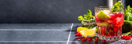 Red currant lemonade or mojito cocktail. Iced fresh summer cocktail with currant berry, lime, miint and ice cubes. Dark tiled background copy spaceの写真素材