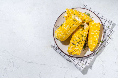 Boiled corn with butter and herbs. Ripe yellow organic cooked corn cobs, on a white kitchen tableの写真素材