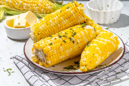 Boiled corn with butter and herbs. Ripe yellow organic cooked corn cobs, on a white kitchen tableの写真素材