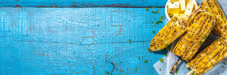 Sweet corn grilled with butter, cheese, cilantro and herbs. Vegetarian, healthy, clean eating barbeque food. Portioned bbq grill corn cobs on high-colored blue wooden backgroundの写真素材