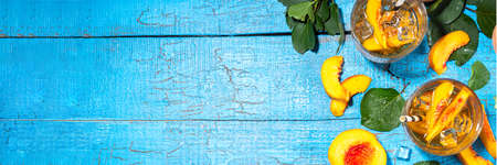 Homemade peach ice tea with ripe fresh peaches on high-colored blue wooden backgroundの写真素材