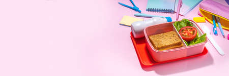 Healthy school meal, back to school concept. Children packed lunch box with balanced diet snack food - yogurt, cereal toast sandwich, apple, fresh vegetable salad, high-colored bright backgroundの写真素材