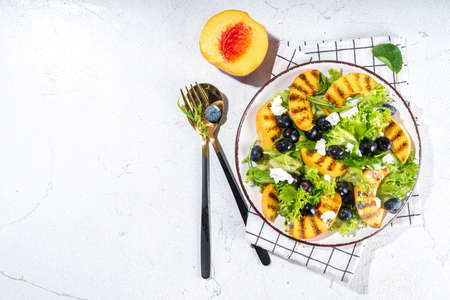 Summer peach salad. Fresh raw green salad with lettuce, arugula, grilled peach wedges, blueberry, feta cheese and honeyの写真素材