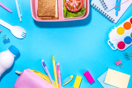 Healthy school meal, back to school concept. Children packed lunch box with balanced diet snack food - yogurt, cereal toast sandwich, apple, fresh vegetable salad, high-colored bright backgroundの写真素材
