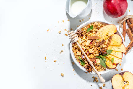 Healthy autumn breakfast granola. Apple pie granola with muesli, cinnamon spices, apples slices, honey and nuts, on white stone background copy spaceの写真素材