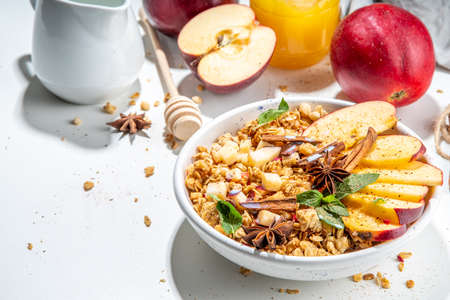Healthy autumn breakfast granola. Apple pie granola with muesli, cinnamon spices, apples slices, honey and nuts, on white stone background copy spaceの写真素材