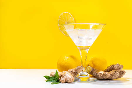 Ginger lemon martini. Sour tasty alcohol cocktail on white and yellow trendy background copy spaceの写真素材