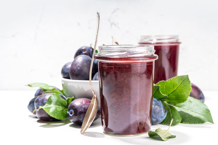 Red blue plum jam in small jar. Homemade autumn plum jam with fresh fruits. Fall preparations and...