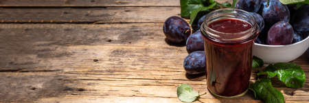 Red blue plum jam in small jar. Homemade autumn plum jam with fresh fruits. Fall preparations and canning on wooden table background copy spaceの写真素材