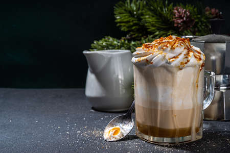 Salted Caramel Brulee Latte. Sweet creamy hot coffe latte drink with whipped cream and caramelized sugar, on dark table background. Autumn winter warm dairy milk coffee beverageの写真素材