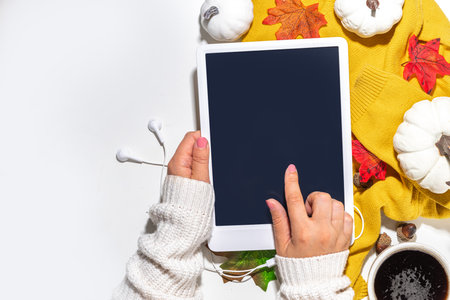 Cozy fall background with coffee cup, tablet notebook, ear-pods, white, orange pumpkins, autumn leaves decor on white home office table background. Autumn still life compositionの写真素材