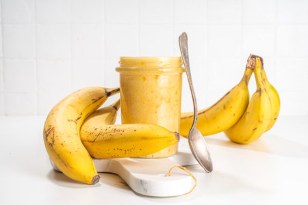 Bananas jam in small glass jar with fresh bananas on white table backgroundの写真素材
