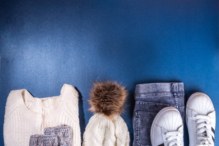 Set of female winter autumn clothes. Jeans, white knitted sweater and hat, mittens and sneakers on dark blue background. Casual cozy fashion outfit flat layの写真素材