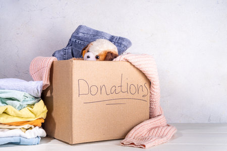 Donation box with clothes, toys and food on white table background. Cardboard donation box full with...