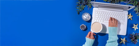 Christmas sale, preparation for holidays concept. winter office workplace background. Laptop, hot chocolate latte cup with Christmas toys, winter tree branches, flat lay on bright blue backgroundの写真素材