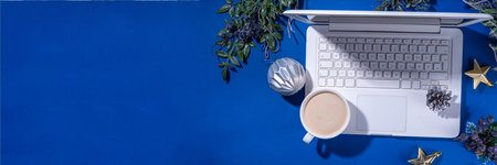 Christmas sale, preparation for holidays concept. winter office workplace background. Laptop, hot chocolate latte cup with Christmas toys, winter tree branches, flat lay on bright blue backgroundの写真素材