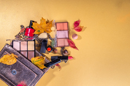 Autumn make up set on golden table background, with autumn leaves and beauty accessories. Various makeup professional cosmetics - shadows, lipstick, corrector, mascara, eyeliner, bronzer, blushの写真素材