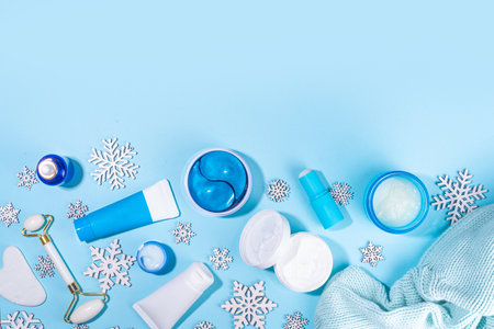 Winter skin care and hand care cosmetic in unbranded containers, bottles, tubes with artificial snowflakes on light blue background. Winter hand skin care cosmetics background top view copy spaceの写真素材
